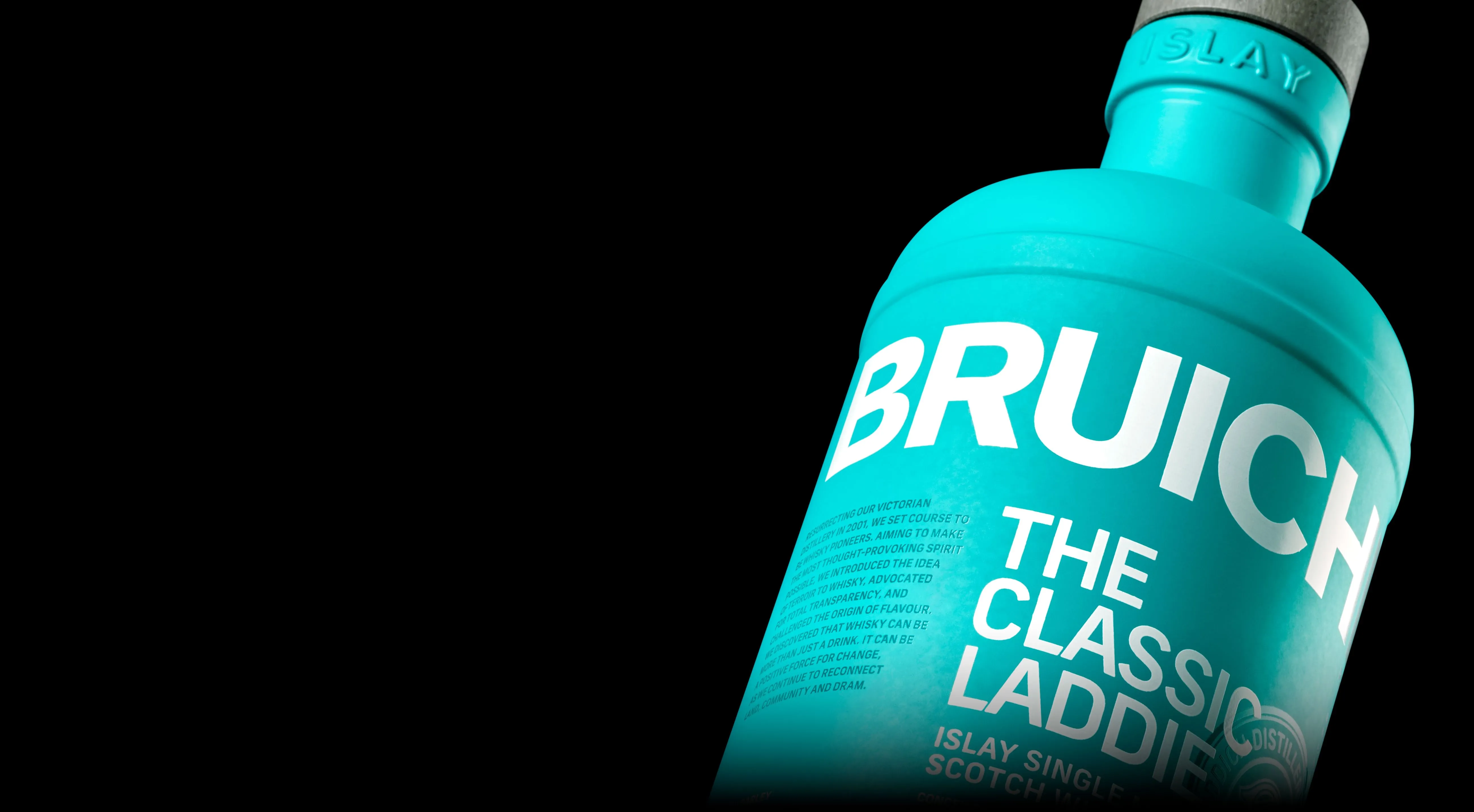 Close up of Bruichladdich bottle on a black background, showcasing bold white typography on clean light matte blue covering the bottle. A subtitle reads The Classic Laddie, Islay Single Malt Scotch Whiskey.
