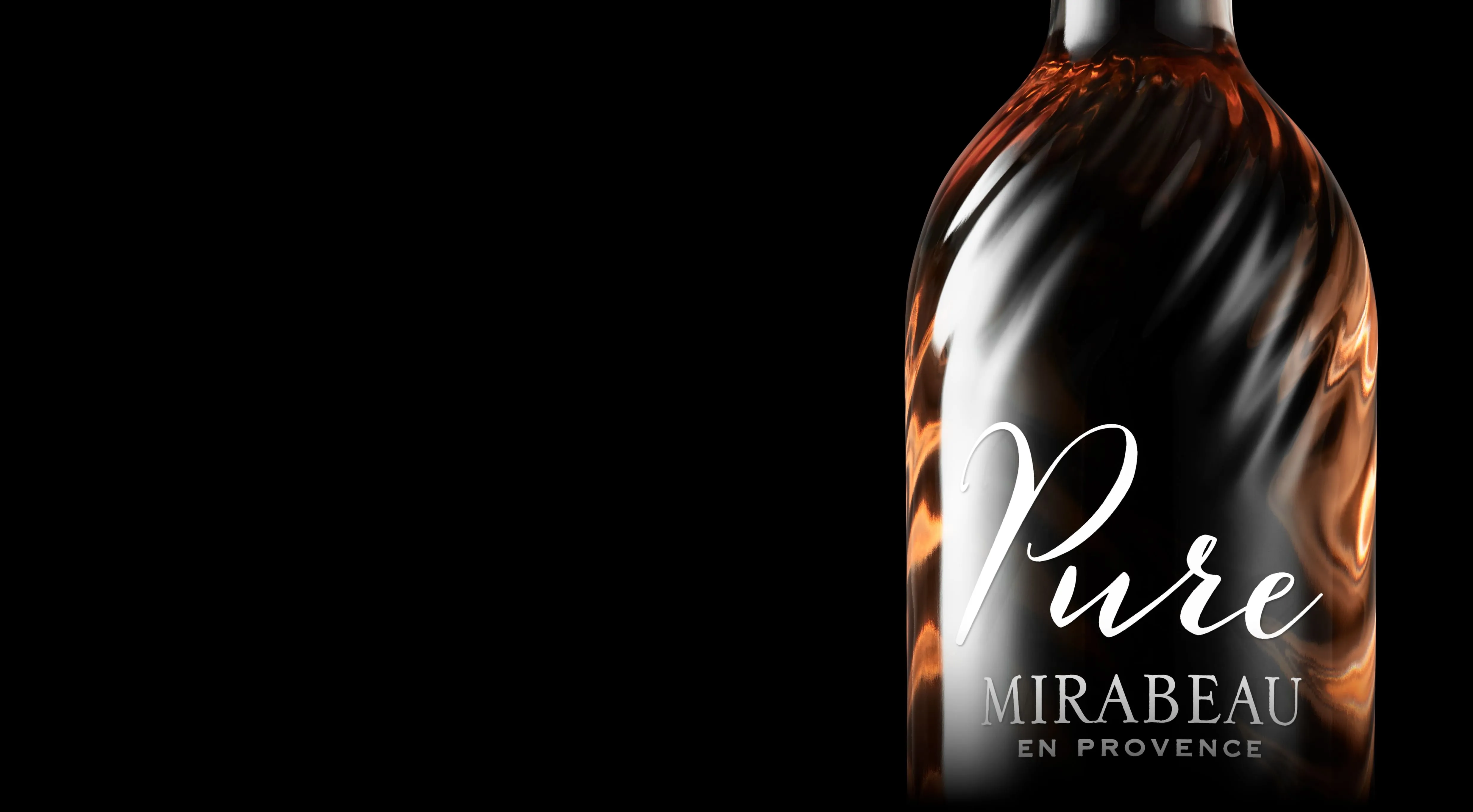Close up of Pure Mirabeau, showcasing the subtle spiral covering the bottles surface. The label of Pure is written in white script with the subtitle Mirabeau En Provence below. Transparent glass shows light coloured liquid in orange and peach hues