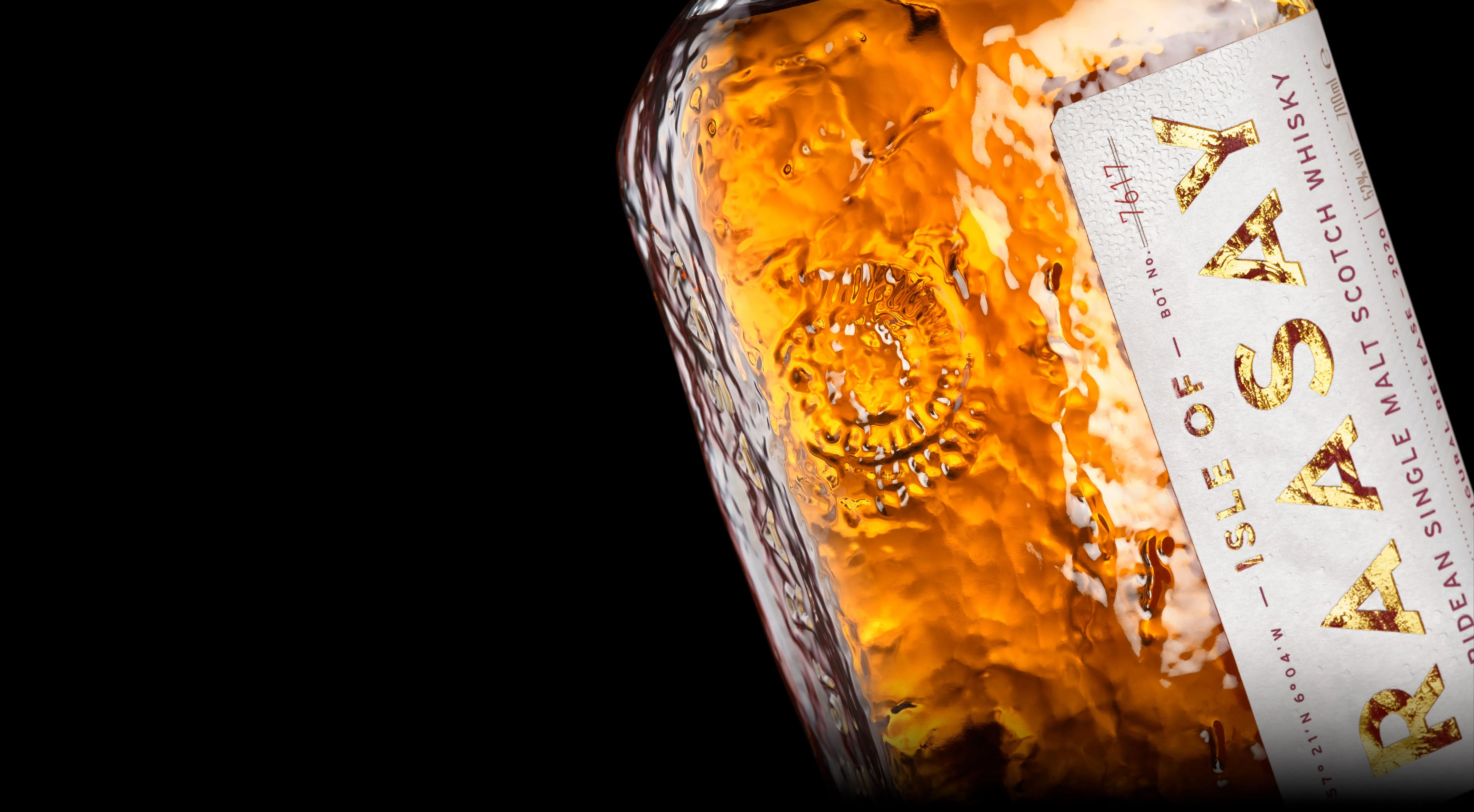 Close up of Isle of Raasay glass bottle showcasing its fossil textured embossing covering the whole surface. Gold text on a textured white label is vertical up the right side of the bottle reads Isle Of Raasay